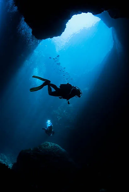 Scuba divers in a sunlit underwater cave